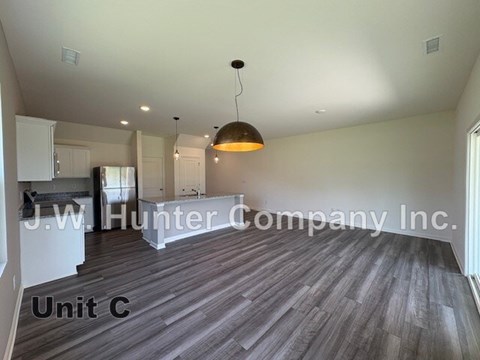 A spacious room with wooden flooring and a hanging light fixture, labeled as Unit C.