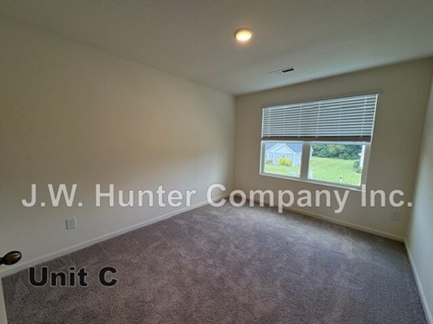 A room with carpet flooring and a window showing a view of a house and trees.