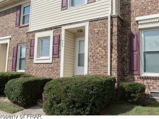 A brick house with a white door and windows with purple shutters.