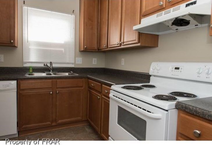 A kitchen with a white stove top oven and wooden cabinets.