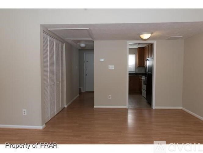 A room with wooden floors and a kitchen visible through the door.