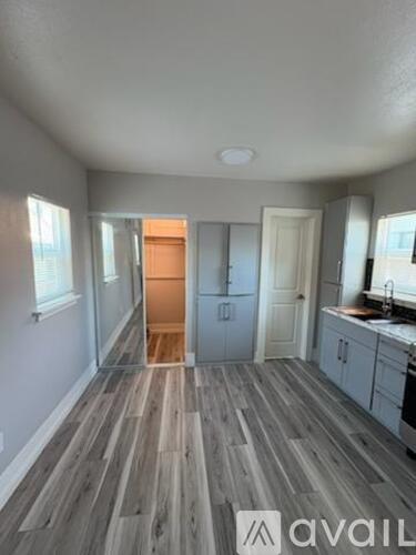 A room with wooden flooring and a kitchen area in the background.