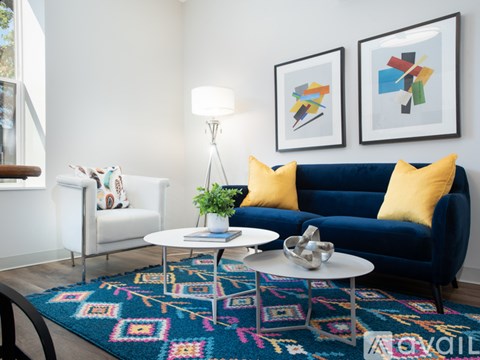 A living room with a blue couch, a white coffee table, and two abstract paintings on the wall.