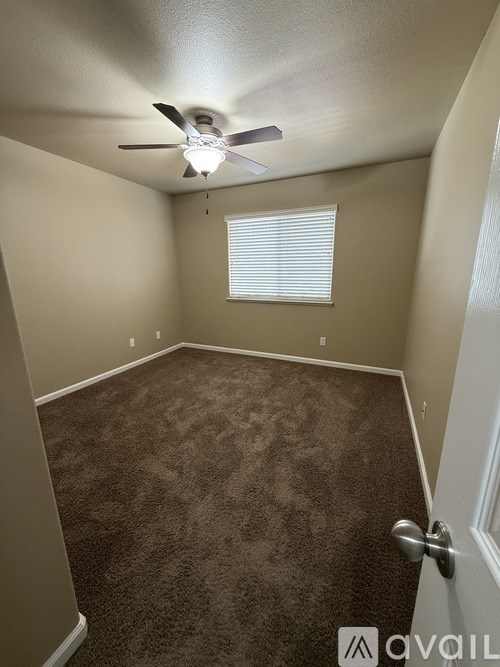 A room with a carpeted floor, a ceiling fan, and a window with blinds.