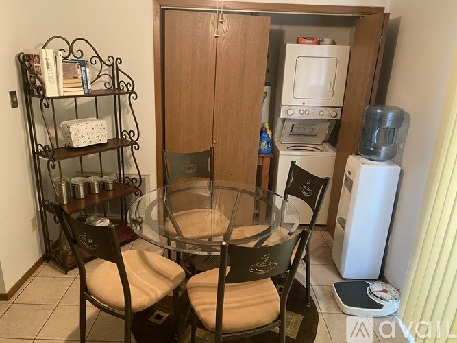 A kitchen with a glass table and chairs, a bookshelf, and a microwave.