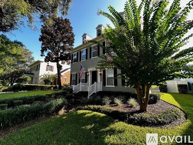 A house with a flag on the front porch is surrounded by a well-manicured lawn and trees.
