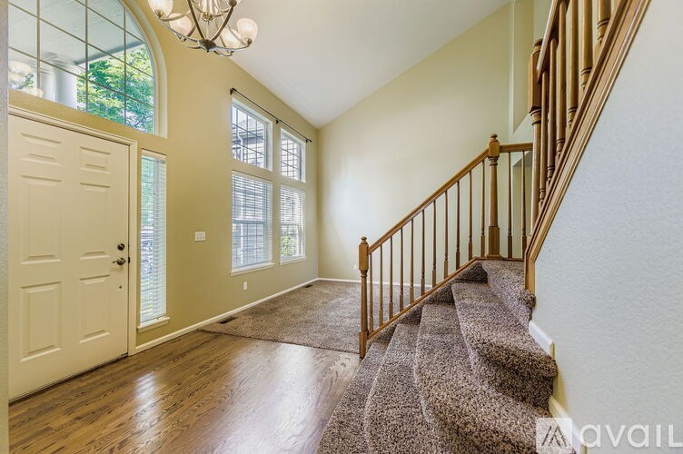 A staircase with a carpeted runner leads up to a landing with a chandelier and a door with a window.