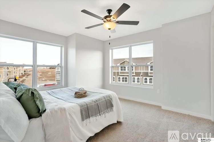 A bedroom with a bed, a ceiling fan, and a window overlooking a residential area.