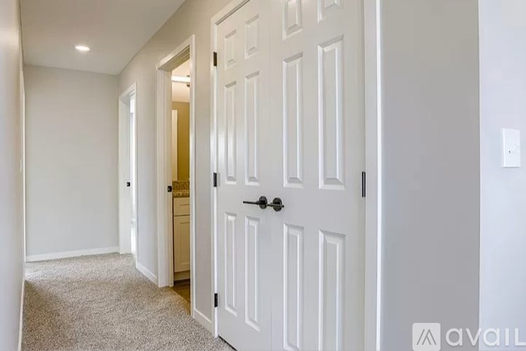 A hallway with a white door and carpeted floor.