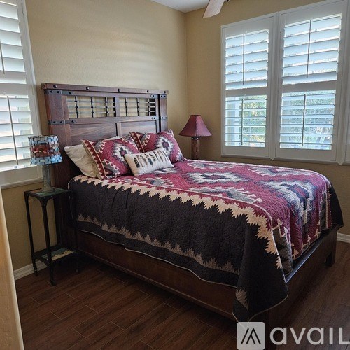 A bedroom with a bed covered in a quilt and a lamp on a side table.