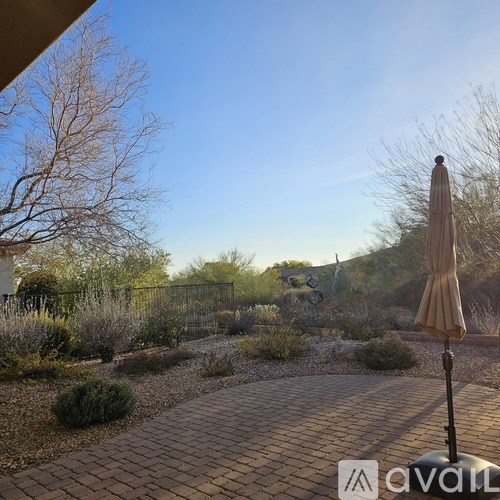 A patio with a beige umbrella and a brick pathway.