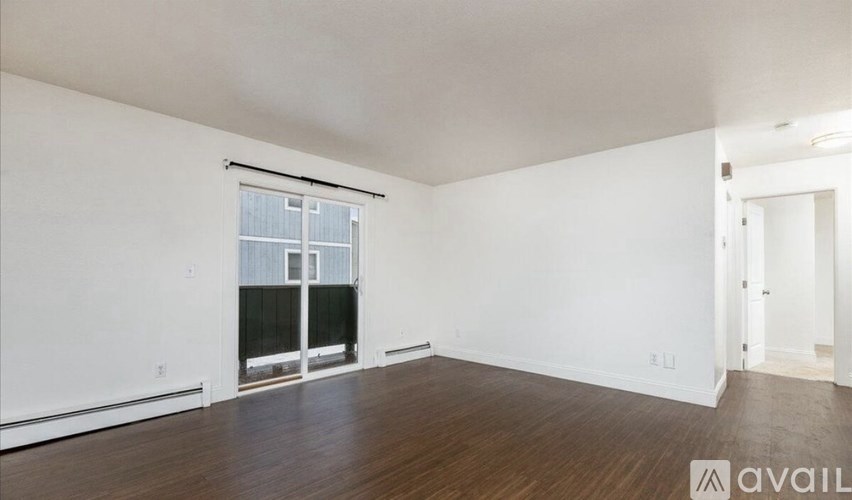 A room with wooden floors and white walls, with a window and a door visible.