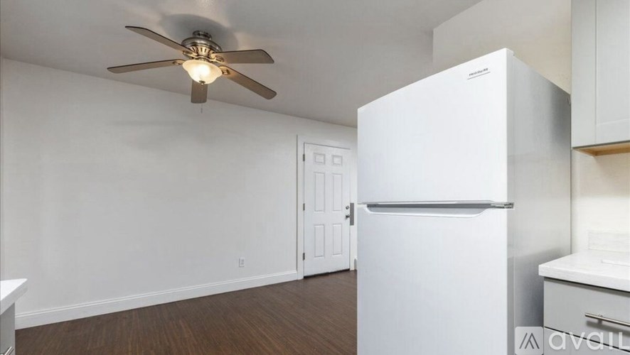 A white refrigerator is in a kitchen with a ceiling fan.
