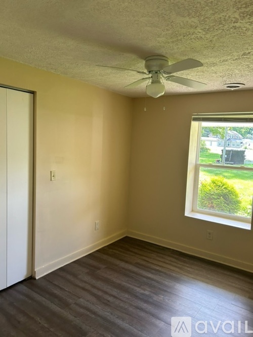 A room with a ceiling fan and a window showing a green lawn outside.