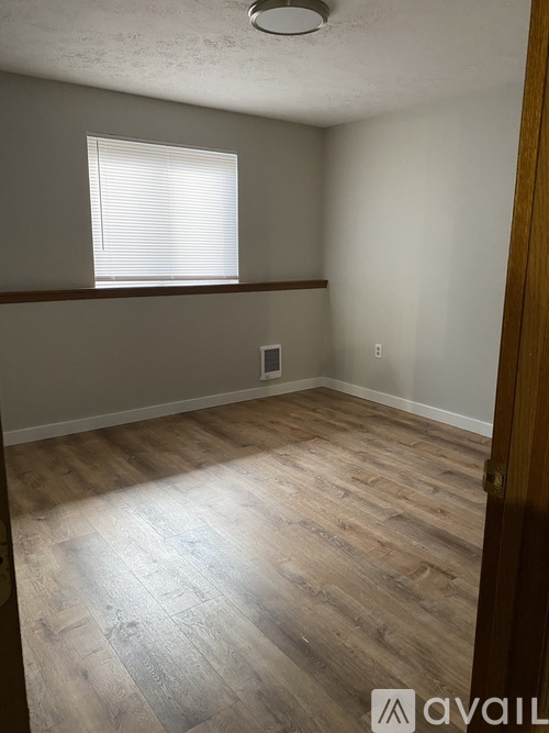 A room with wooden flooring and a window with blinds.