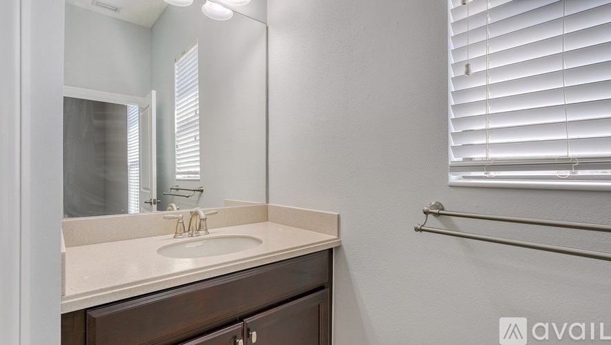A bathroom with a sink, mirror, and a window with blinds.