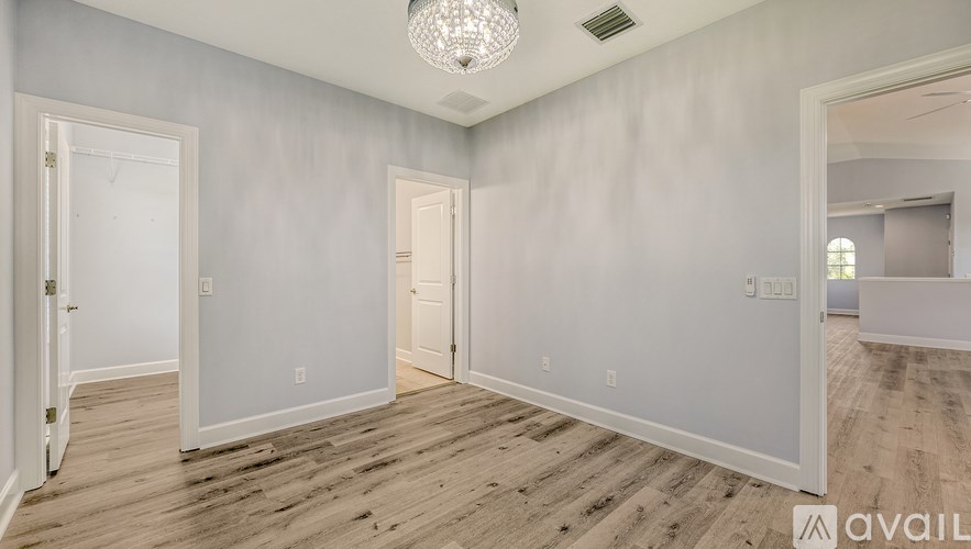 A spacious room with wooden flooring and a chandelier hanging from the ceiling.