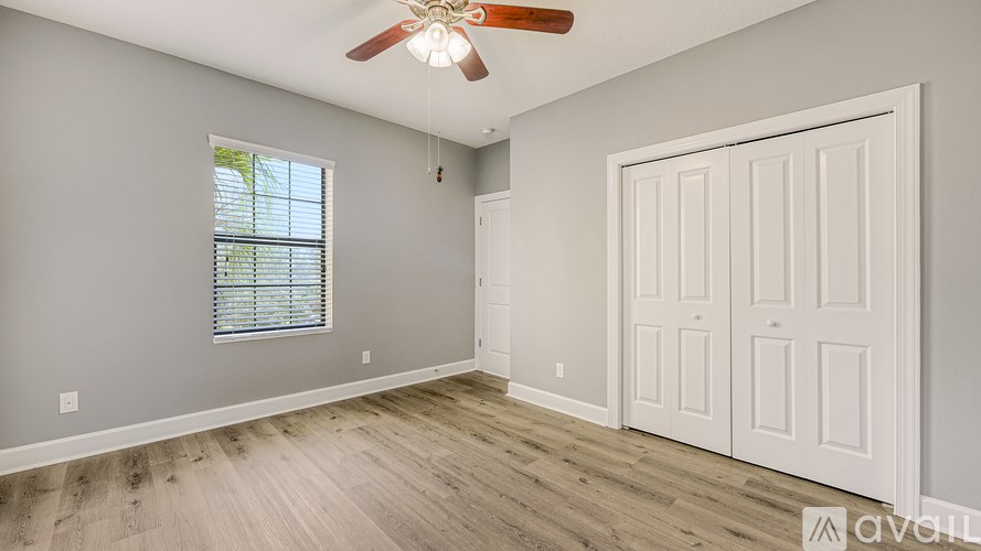 A room with a white door, a ceiling fan, and a window with blinds.