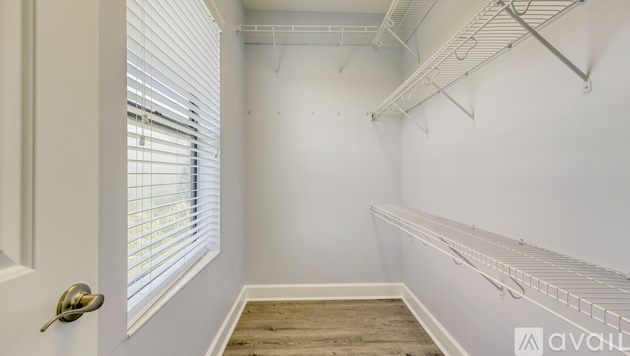 A room with a door, a window with blinds, and a wall with a shelf.