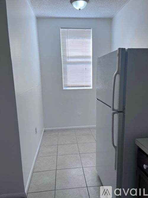 A kitchen with a refrigerator and a window with blinds.