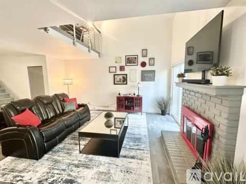 A black leather sofa with red pillows sits in a living room with a fireplace and a television.