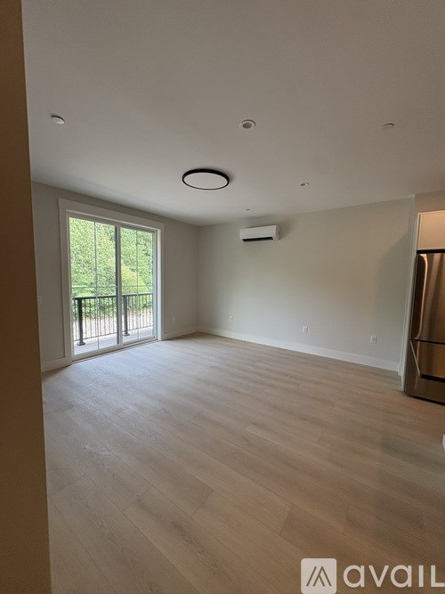 A spacious room with wooden flooring and a sliding glass door leading outside.