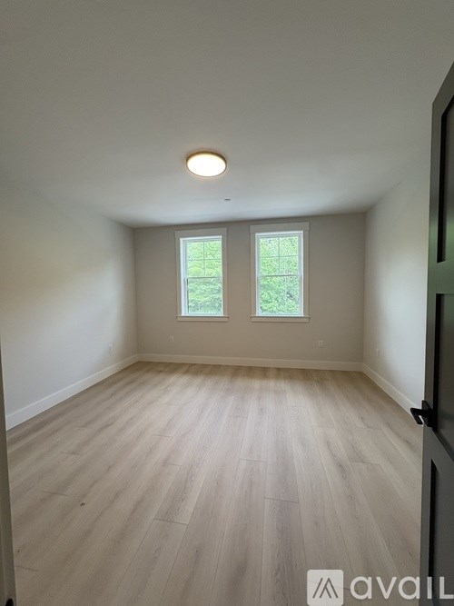 A room with light wood flooring and two windows.