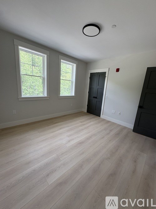 A room with wooden flooring and two windows.