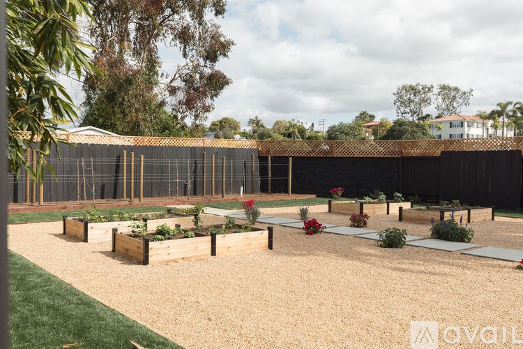 A sandy garden area with a fence and flower beds.