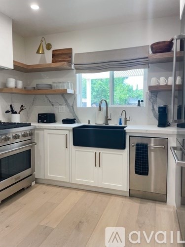 A kitchen with white cabinets and a wooden shelf above the stove.