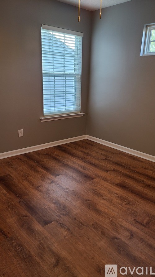 A room with wooden flooring and a window with blinds.