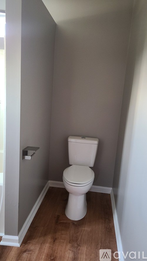 A white toilet in a small bathroom with wood flooring.