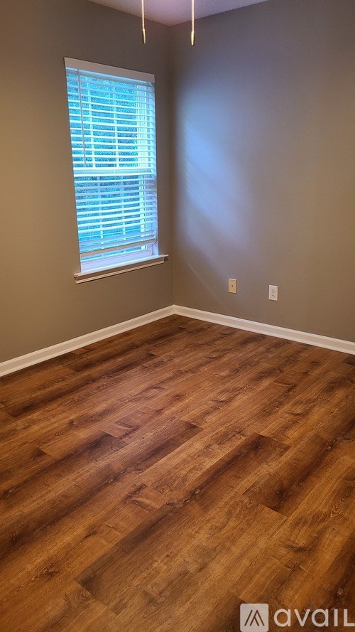 A room with wooden flooring and a window with blinds.