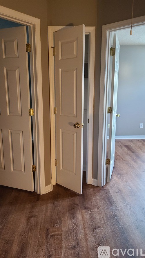 Three white doors with brass knobs are open in a room with wood flooring.