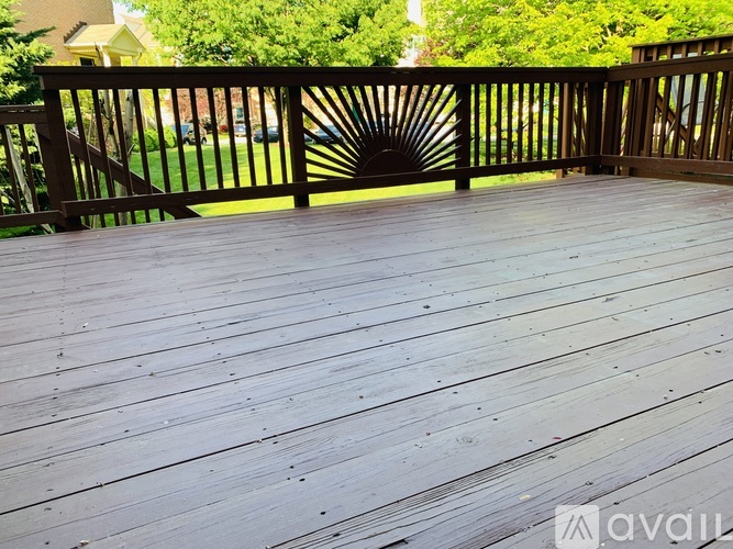 A wooden deck with a railing and a view of a lawn and trees.