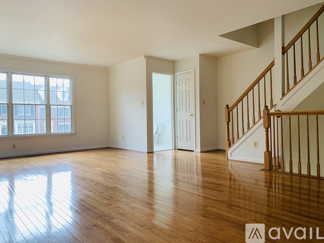 A spacious room with wooden floors and a staircase on the right side.