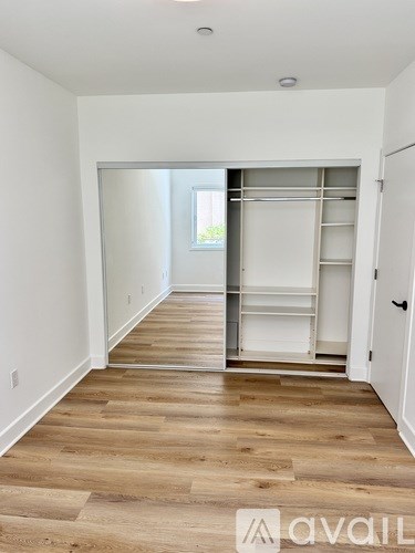 A room with wooden flooring and a white wall with a doorway leading to another room.