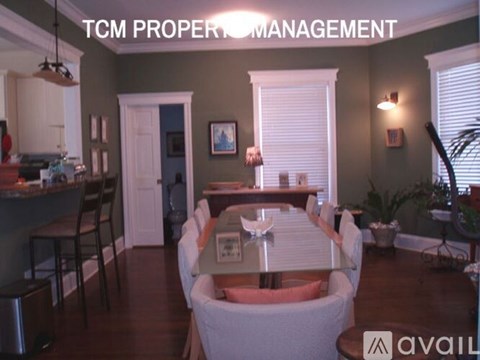 A living room with a dining table and chairs, and a kitchen area in the background.
