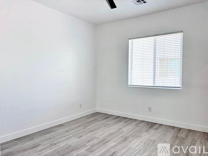 A room with a window covered by white blinds and wooden flooring.