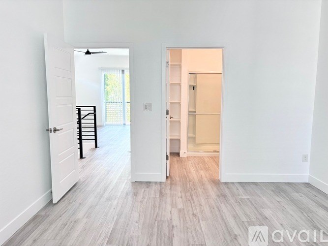 A room with white walls and a wooden floor with a doorway leading to another room.