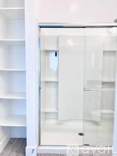 A white bathroom with a walk in shower and shelves.