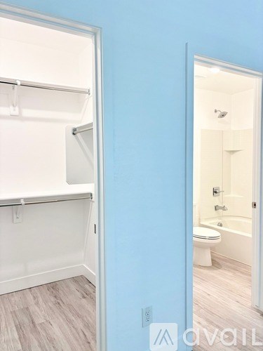 A white closet with a mirrored door is open to a bathroom with a toilet and tub.