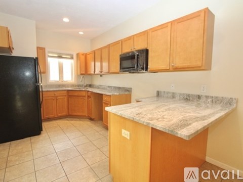 A kitchen with black fridge, brown cabinets and a marble counter top.