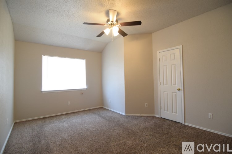 A room with a carpeted floor, a ceiling fan, and a large window with blinds.