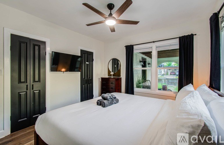 A bedroom with a large bed, a ceiling fan, and a window with curtains.