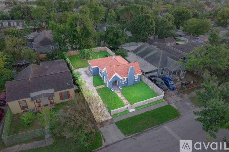 A house with a red roof is surrounded by other houses and trees.