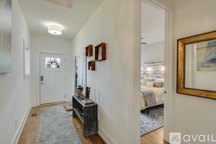 A hallway with a rug, a wooden table with a vase and candles, and a mirror on the wall.