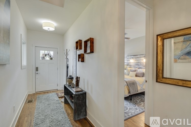 A hallway with a rug, a wooden table with a vase and candles, and a mirror on the wall.