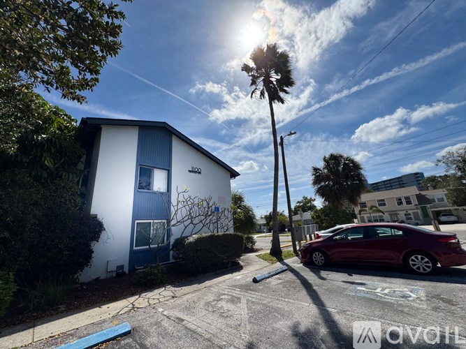 A red car is parked on the street in front of a white and blue house.