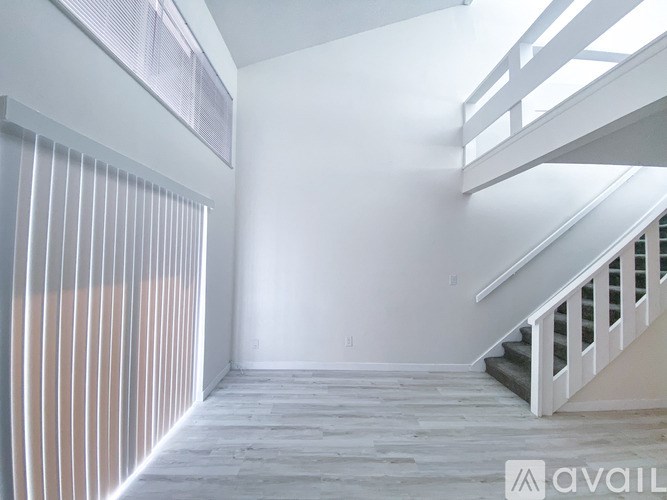 A spacious room with a staircase and a window with vertical blinds.